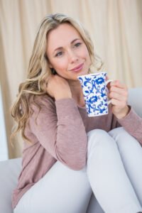 Thoughtful blonde on couch holding cup of coffee at home in the living room